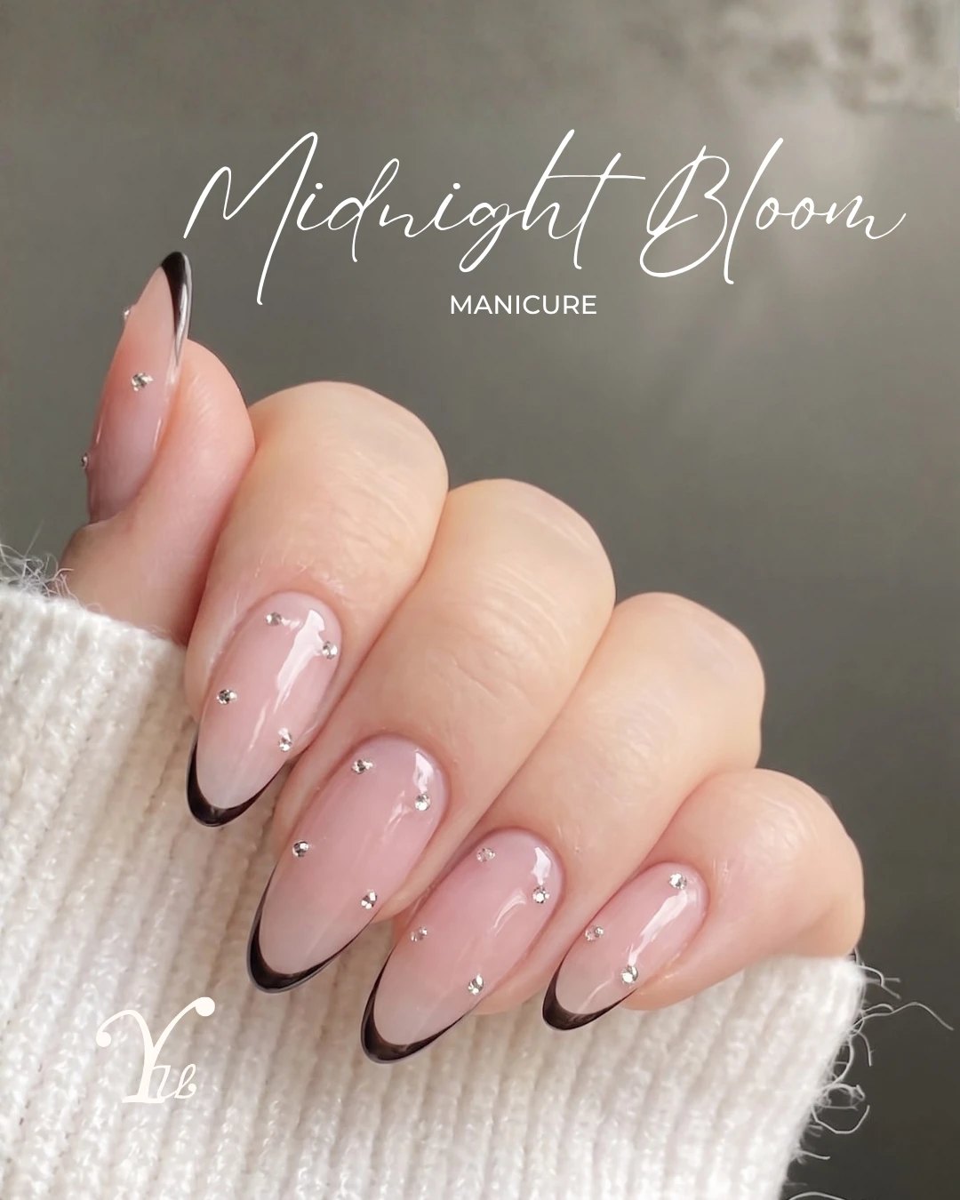 Almond nails with a black French tip and scattered crystals, against a cream knit sleeve